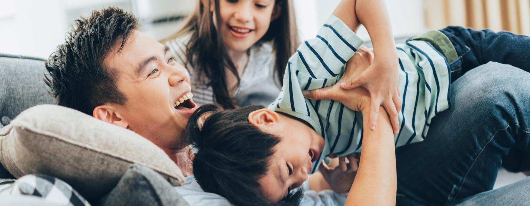 father plays on a couch with his young children